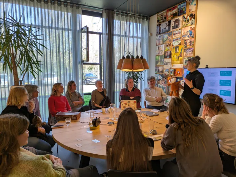 Bijeenkomst Empower The Young. Het team zit aan tafel en krijgt een demonstratie van een Tellmie.